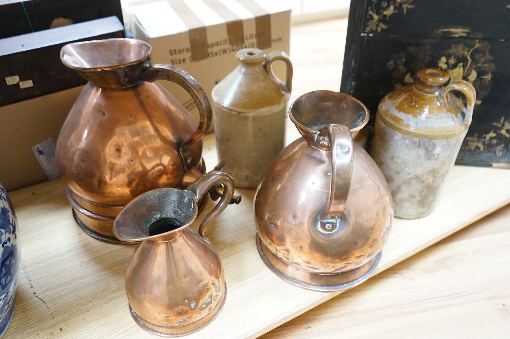 Three graduated copper haystack measures, H 39cm x W 40cm (inc spout), H 35cm x 25cm and H25cm x 18cm, Three stoneware jars H 32cm x W 20cm (two jars), H 20cm x W 16cm (1 jar)